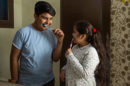 Portrait of happy siblings brushing teeth together in front of mirror at home