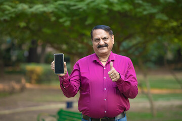 indian man showing smartphone screen at park.