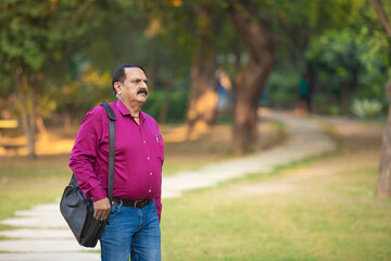 Indian man holding laptop bag and walking at park.