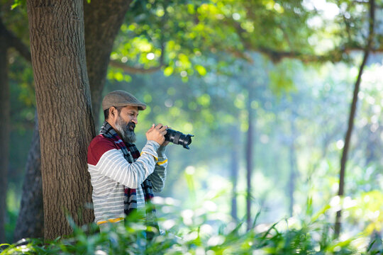 Indian man taking some photo and using camera at garden