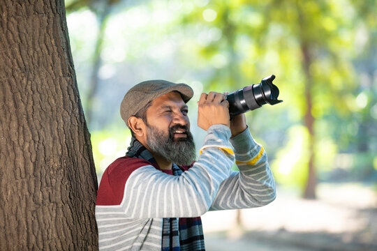 Indian man taking some photo and using camera at garden
