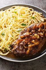 Traditional dry aged roast beef with fried onion rings and Swabian spaetzle closeup on the plate on the table. Vertical