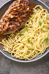 Zwiebelrostbraten it is a festive dish of beef with fried onions arranged on top served with spaetzle closeup on the plate on the table. Vertical top view from above
