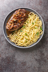 Traditional dry aged roast beef with fried onion rings and Swabian spaetzle closeup on the plate on the table. Vertical top view from above