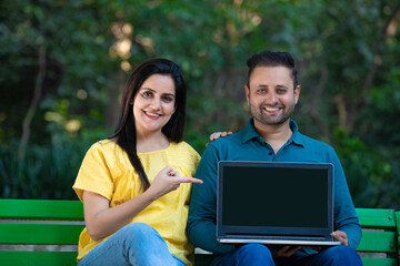 Young indian couple showing laptop screen at park.