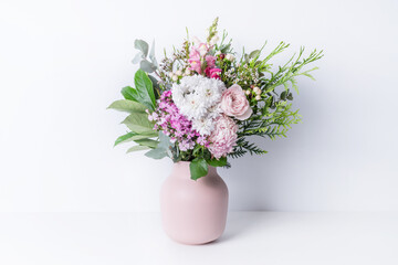 Beautiful cottage style flower arrangement, in a pink vase, on a white table. Flower bunch include Rose, Snapdragon, Ranunculus, Daisy's, Sweet William, Chrysanthemum and lush green foliage. 