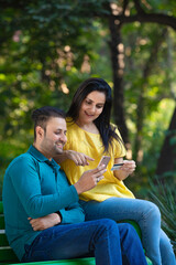 Fototapeta premium Indian man and woman using smartphone and bank card at park.