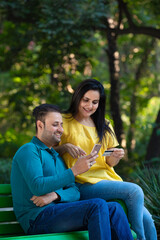 Fototapeta premium Indian man and woman using smartphone and bank card at park.