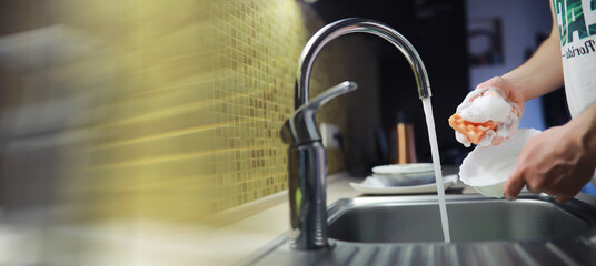 People are washing the dishes . Cleaning solution.A white bottle with dishwashing gel, sponges and rubber gloves on the background of a sink with dirty dishes.