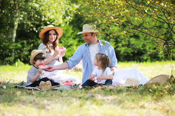 Happy family with children having picnic in park, parents with kids sitting on garden grass and eating watermelon outdoors