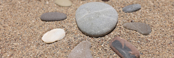 Fototapeta na wymiar Figure of sun is made of pebble stones on sandy beach in summer