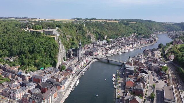 Scenic summer view of Dinant cityscape on banks of river Meuse overlooking Collegiate Church of Notre Dame and fortified Citadel on top of cliff overgrown with green trees, Namur province, Belgium
