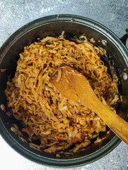 Braised cabbage in a pan on a gray background with a wooden spatula. Close up 