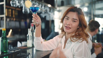 A young woman drinking cocktail sitting at bar in restaurant looking at camera