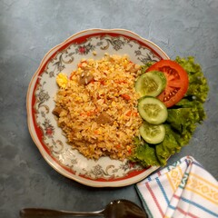 Top view of fried rice “nasi goreng” with slice of cucumber, tomatoe and lettuce at the plate of red flower motive in the kitchen