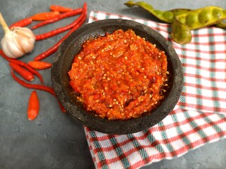 closeup spicy sambal in the stone mortar with red chili and garlic in the grey backround and duster at the kitchen