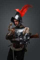 Portrait of medieval musketeer man with plate armor and sword isolated on grey.