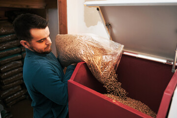 Bearded man puts wood pellet from the bag into the heating boiler oven. Sustainable future concept.