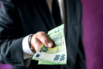 man in a suit and shirt counts the euro bills he received for the work done in the office.