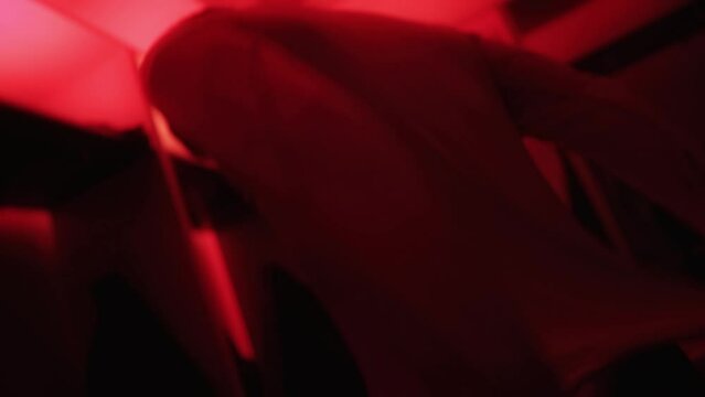Football team player puts a jersey T-shirt on his body in dark locker room before start of soccer match. Man changes into sport uniform in dressing room with red lighting. Cloakroom. Shaky shot