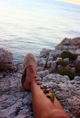 Relaxing moment watching the sunset in a cliff. Sunbathed leg decorated with stones.