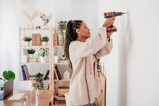 Woman using drill machine on wall at home