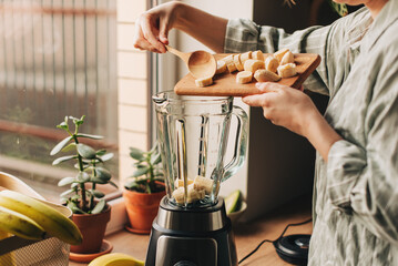 Woman is preparing a healthy detox drink in a blender - a green smoothie with fresh fruits, green...