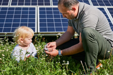 Father showing to his little son how to use tools in background of solar panels. Dad teaching his...