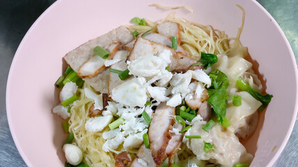 Asian yellow Noodles, pork and crab meat, dumplings and veggies in pink bowl.