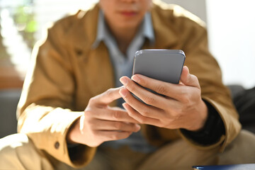 Selective focused on hands. Man chatting online in social network on smart phone while sitting on couch at home