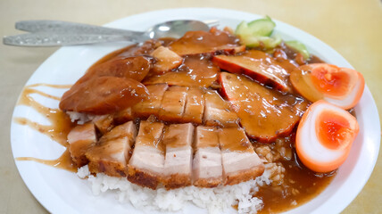 a plate of roasted red pork, crispy pork, and a perfectly half-boiled egg served atop a bed of steaming white rice, combined with the crunch of the crispy pork and the rich yolk