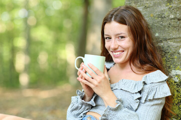 Happy woman looks at you holding coffee mug outside