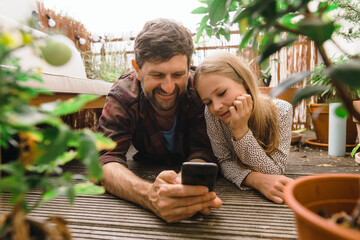 Father sharing smart phone with daughter lying in balcony