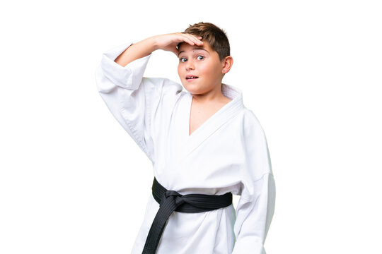Little caucasian kid doing karate over isolated chroma key background doing surprise gesture while looking to the side