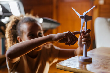 Girl rotating blade of wind turbine model on table at home