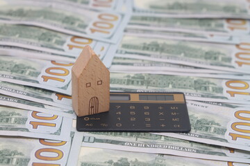House model and a calculator on the background of dollar banknotes. The concept of buying and selling real estate.