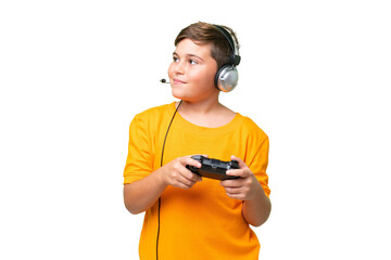 Little caucasian kid playing with a video game controller over isolated chroma key background looking to the side and smiling © luismolinero