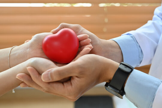 Cropped image of doctor and patient hands holding red heart shape. Health care, organ donation and cardiology concept