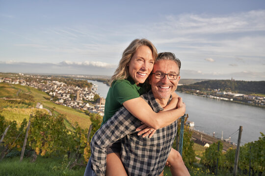 Happy man piggybacking woman by river on hill - Powered by Adobe