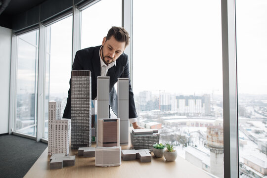 People, global business, company worker concept. Portrait of confident bearded businessman real estate agent in formal clothes, looking at building complex prototype project of 3d city model at table