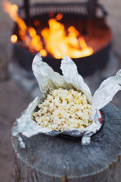 Popcorn in an aluminium foil keeps on a heater on a wood log to fry.
