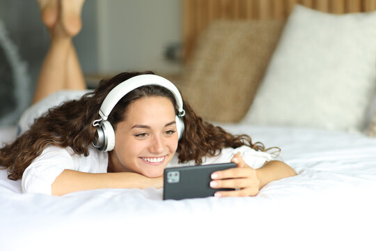 Happy Woman Watching Videos On Smart Phone On A Bed