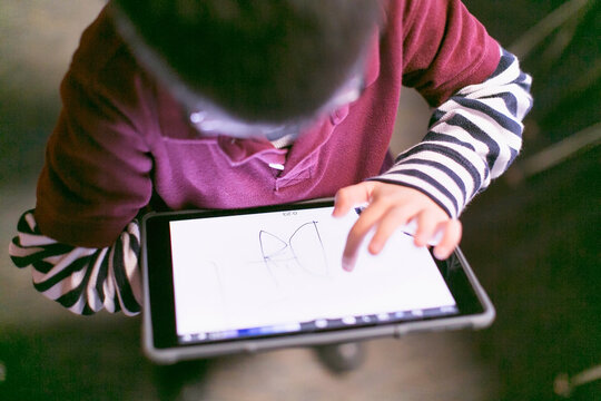 A cute little boy with eyeglasses practice his lesson on his tablet.