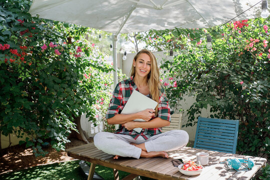 Happy freelancer sitting with laptop on table in back yard