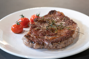 Cooked and grilled steak on white dish with a little tomato with it, ready for the next decoration step.