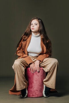 Teenage girl sitting on stool against gray background