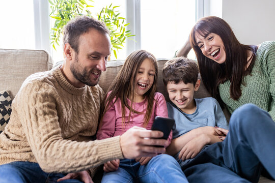 Cheerful family using smart phone on sofa in living room