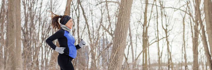 Pregnant woman running in winter during Pregnancy. Female runner jogging in winter forest wearing warm running clothing. Beautiful fit fitness model and expectant mother. Panoramic banner