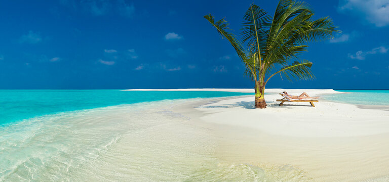 Woman lounging underneath palm tree on small island