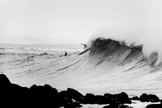 Surfer on wave rolling to rocky shore